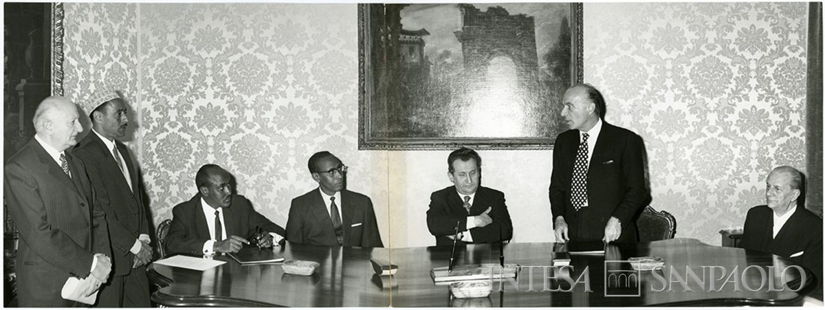 Firma per la costituzione della Somali Savings and Credit Bank (Cassa di Risparmio somala), 4 marzo 1971 (Fotografia Pontificia Giordani). Da sinistra: Falaguerra Luigi, tre persone n.i. (tra i somali presenti, vi erano l'ambasciatore somalo, il collega somalo di Carli Abdurahman Herzii e il direttore generale del nuovo istituto somalo Scerif Zen), il sottosegretario Pedini Mario, il governatore della Banca d'Italia Carli Guido, Dell'Amore Giordano