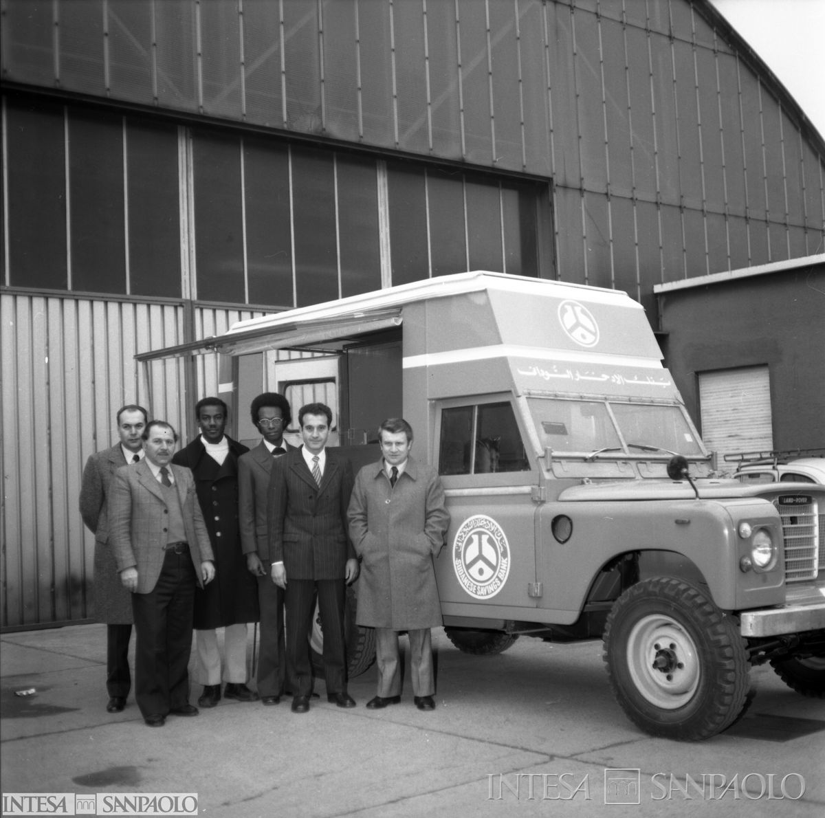 Unità mobile della Sudanese Savings Bank ripresa a Milano, prima della partenza, con gruppo di persone davanti in posa, ante agosto 1975 (fotografo sconosciuto)