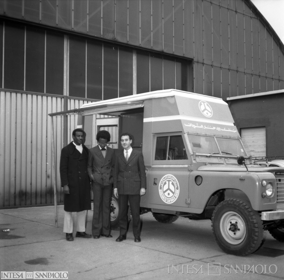 Unità mobile della Sudanese Savings Bank ripresa a Milano, prima della partenza, con gruppo di persone davanti in posa, ante agosto 1975 (fotografo sconosciuto)