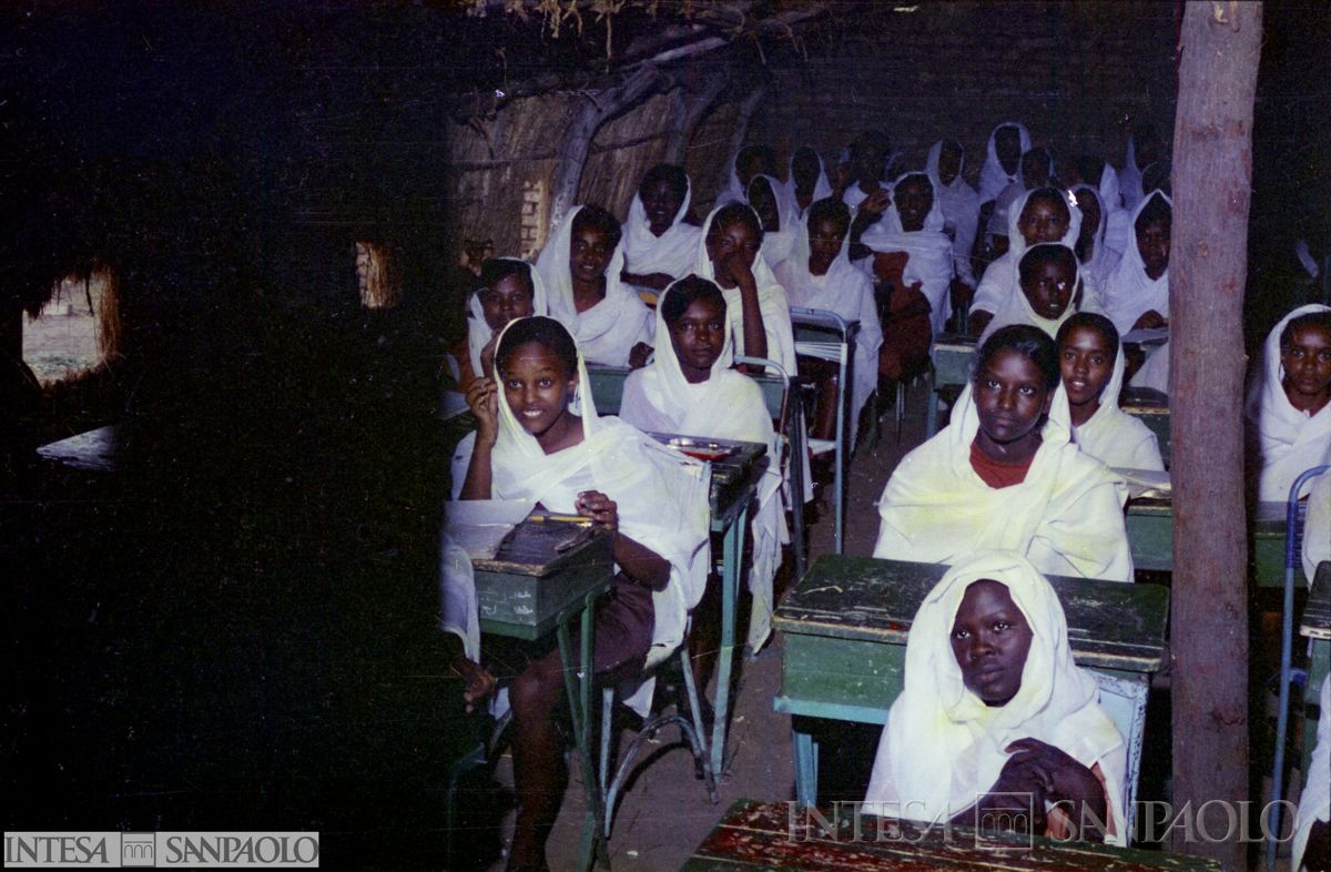 Donne sedute a dei banchi in una capanna, probabilmente adibita a luogo di istruzione, post agosto 1975 (fotografo sconosciuto)