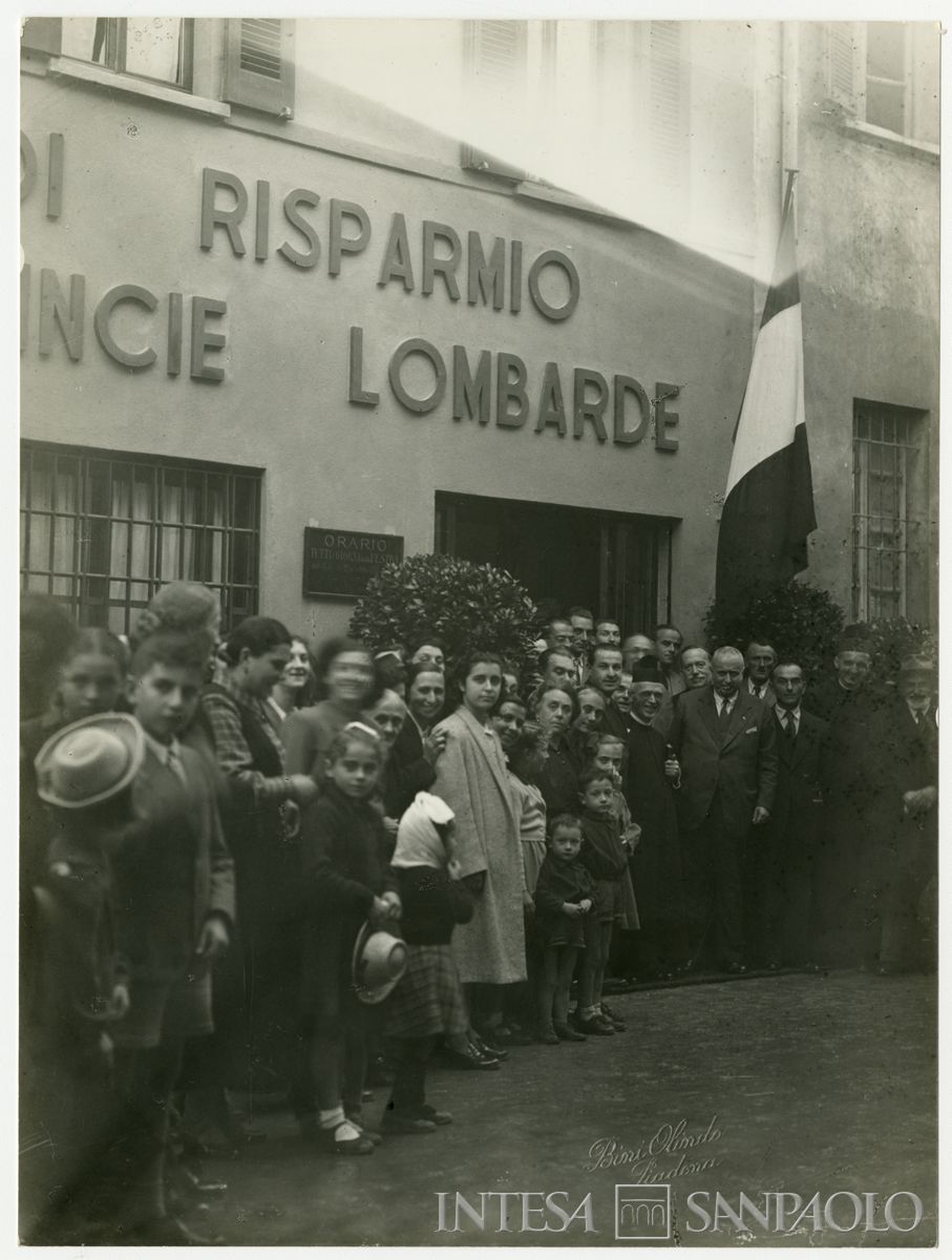 Foto di gruppo all'esterno della filiale Cariplo di Isola Dovarese, il giorno dell'inaugurazione; a destra del parroco il presidente Stefano Jacini, ottobre 1948 (Olindo Bini)