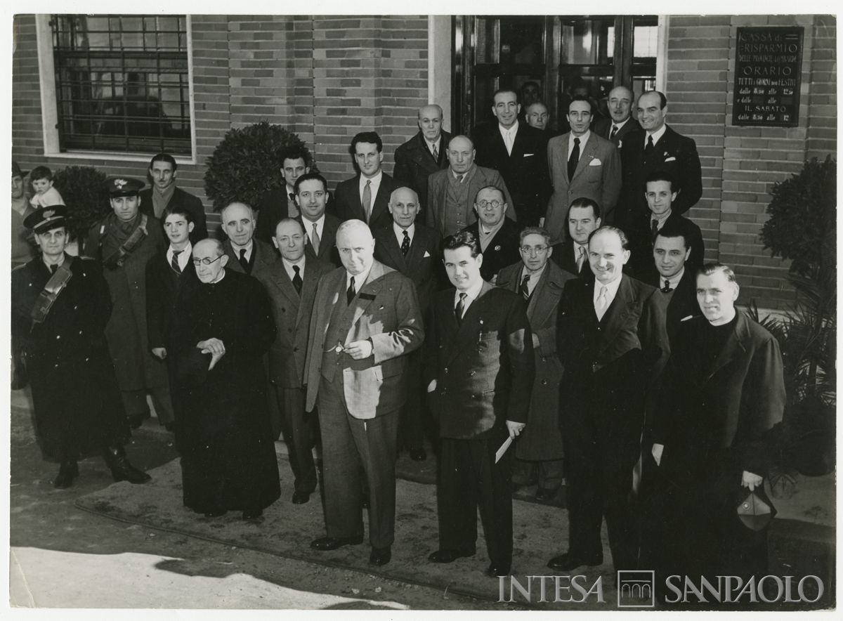 Foto di gruppo all'esterno della filiale Cariplo di Parabiago, in via S. Michele 5, il giorno dell'inaugurazione; al centro in prima fila il presidente Stefano Jacini, alla sua destra dietro il parroco, il vice presidente Cesare Chiodi, 7 marzo 1948 ("Terreni" Attualità fotografica "Reporter")
