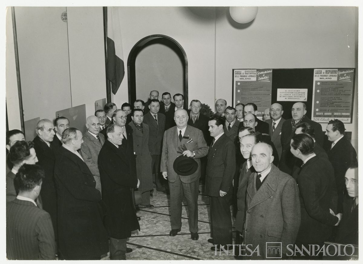 Foto di gruppo all'interno della filiale Cariplo di Parabiago, in via S. Michele 5, il giorno dell'inaugurazione; al centro, vestito di chiaro, il presidente Stefano Jacini, 7 marzo 1948 ("Terreni" Attualità fotografica "Reporter")