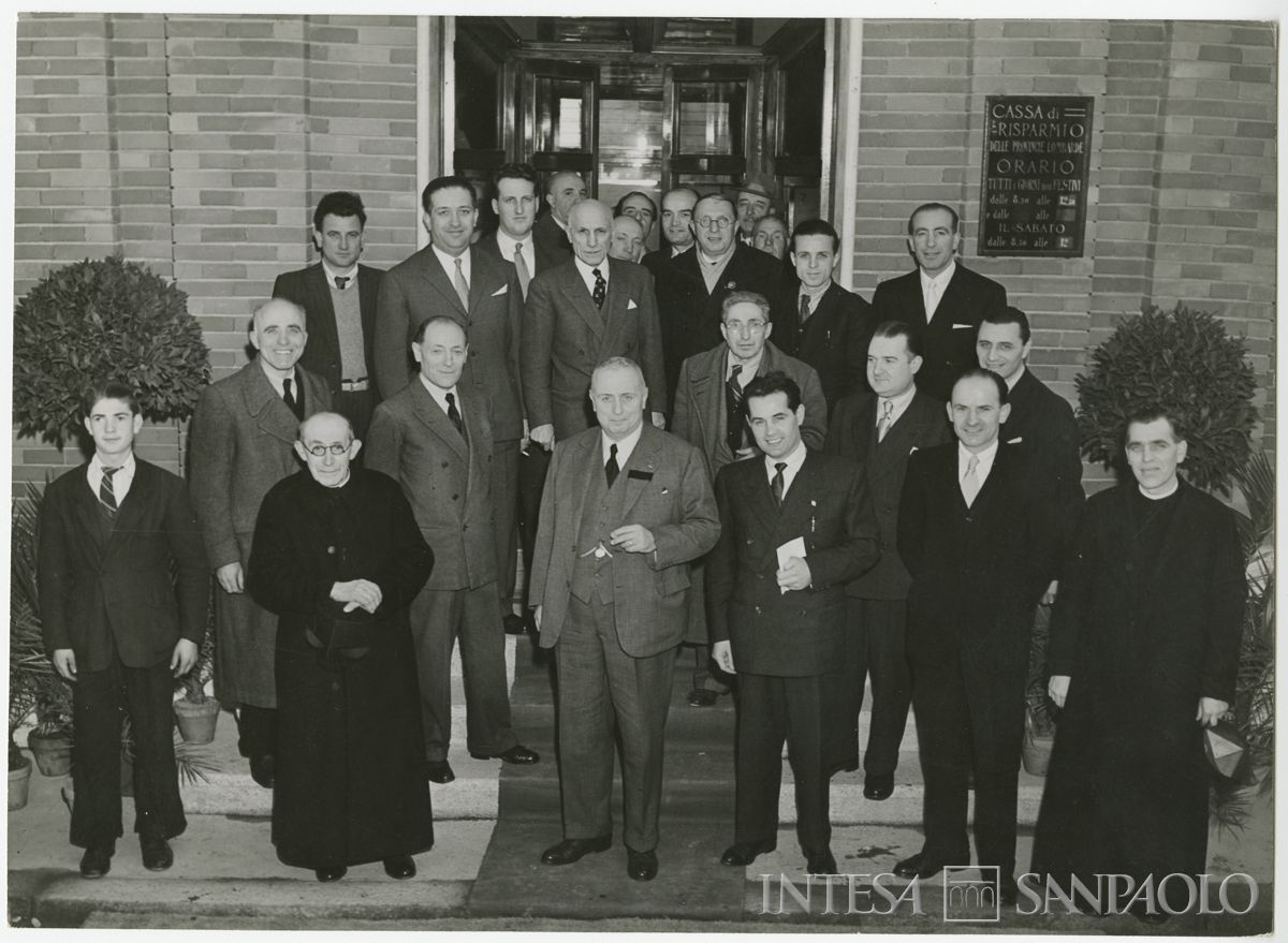 Foto di gruppo all'esterno della filiale Cariplo di Parabiago, in via S. Michele 5, il giorno dell'inaugurazione; al centro in prima fila il presidente Stefano Jacini, alla sua destra dietro il parroco, il vice presidente Cesare Chiodi, 7 marzo 1948 ("Terreni" Attualità fotografica "Reporter")
