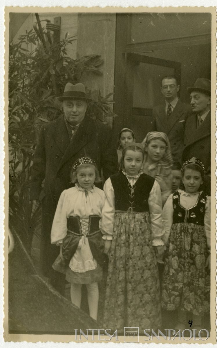 Il presidente Cariplo Stefano Jacini, a sinistra, con bambine in abiti tradizionali all'inaugurazione della filiale di Mariano Comense; dietro da destra il direttore generale Gian Luigi Dones e Sandro Candiani, [1950] (fotografo sconosciuto)