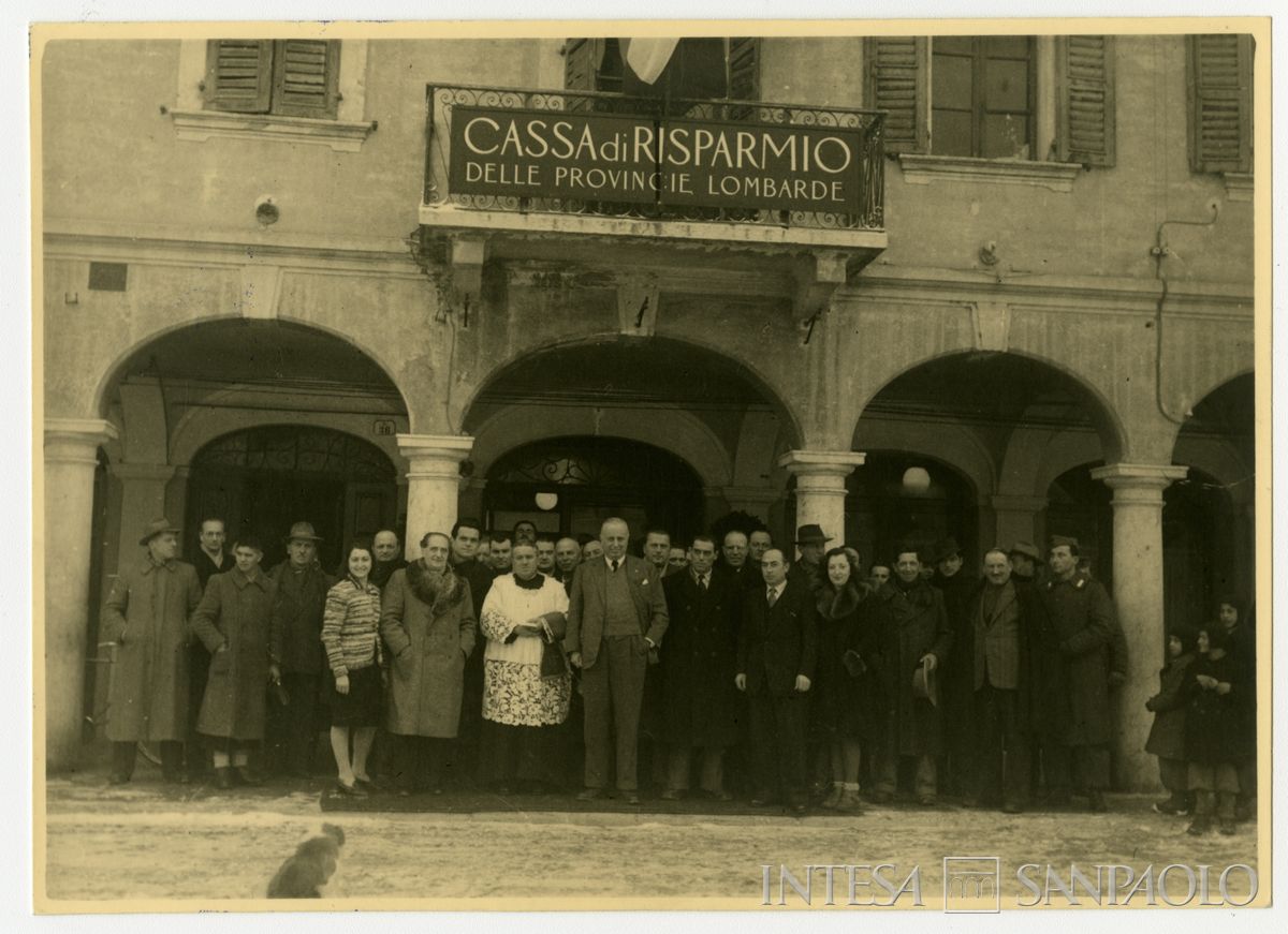 Foto di gruppo all'esterno della filiale Cariplo di Gonzaga il giorno dell'inaugurazione; in prima fila a destra  del parroco il presidente Stefano Jacini, 10 gennaio 1947 (fotografo sconosciuto)