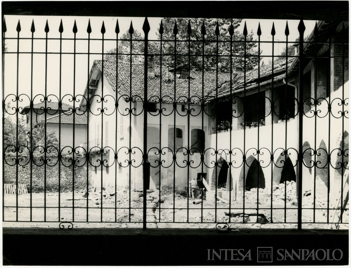 Ganna, Badia di San Gemolo: esterno del chiostro gotico della Badia, fotografato da dietro un cancello, durante il restauro, 1964 (Fotografia E. Malnati)