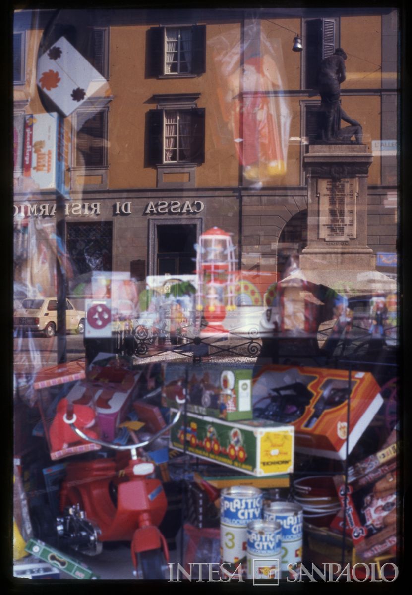 Cariplo, la filiale di Sarnico riflessa in una vetrina di giocattoli, [1975] (Tito Terzi)