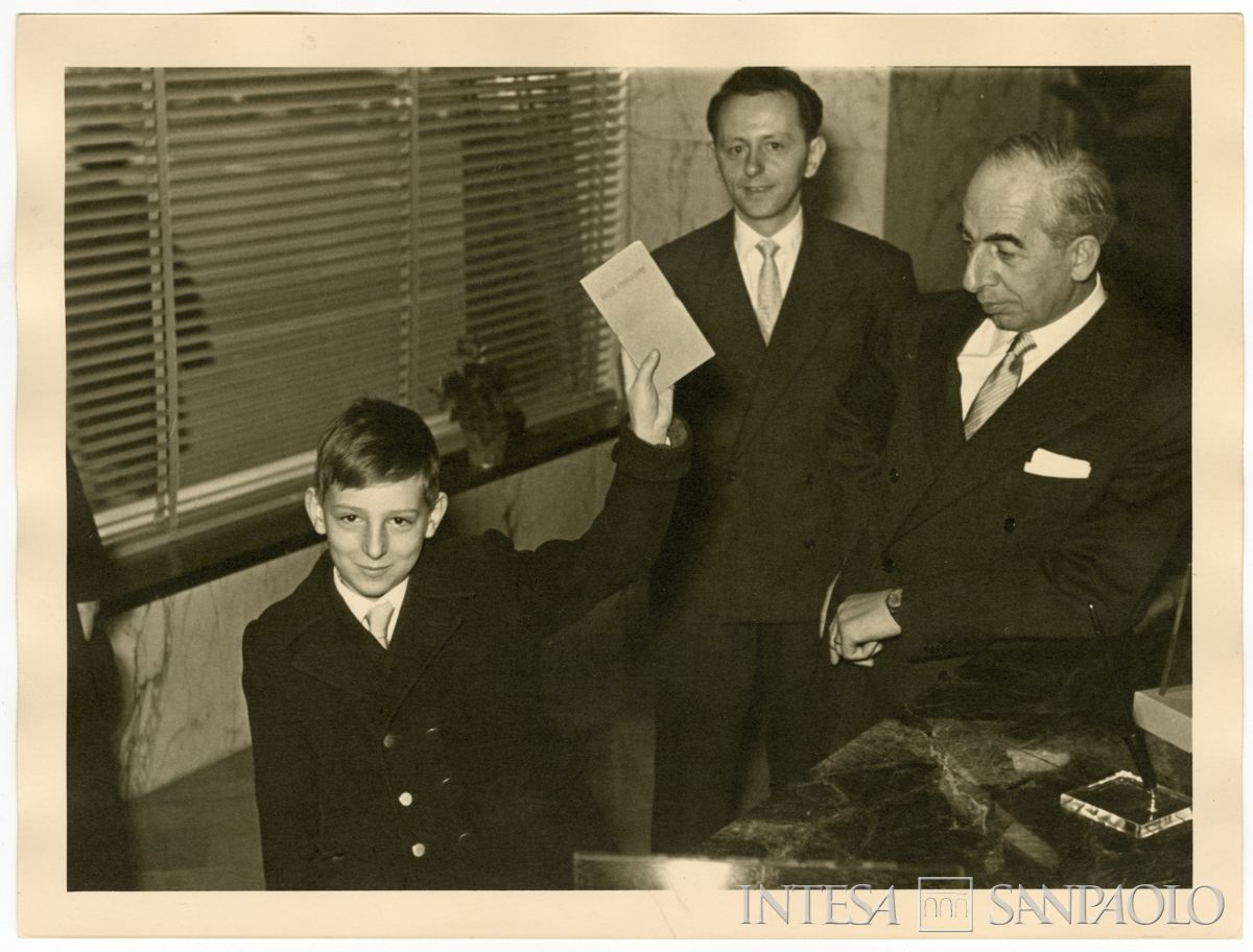 Bambino con il libretto di risparmio ricevuto durante l'inaugurazione dell'agenzia n. 15 di piazza della Repubblica del Banco Ambrosiano, 8 dicembre 1955 (fotografo sconosciuto)