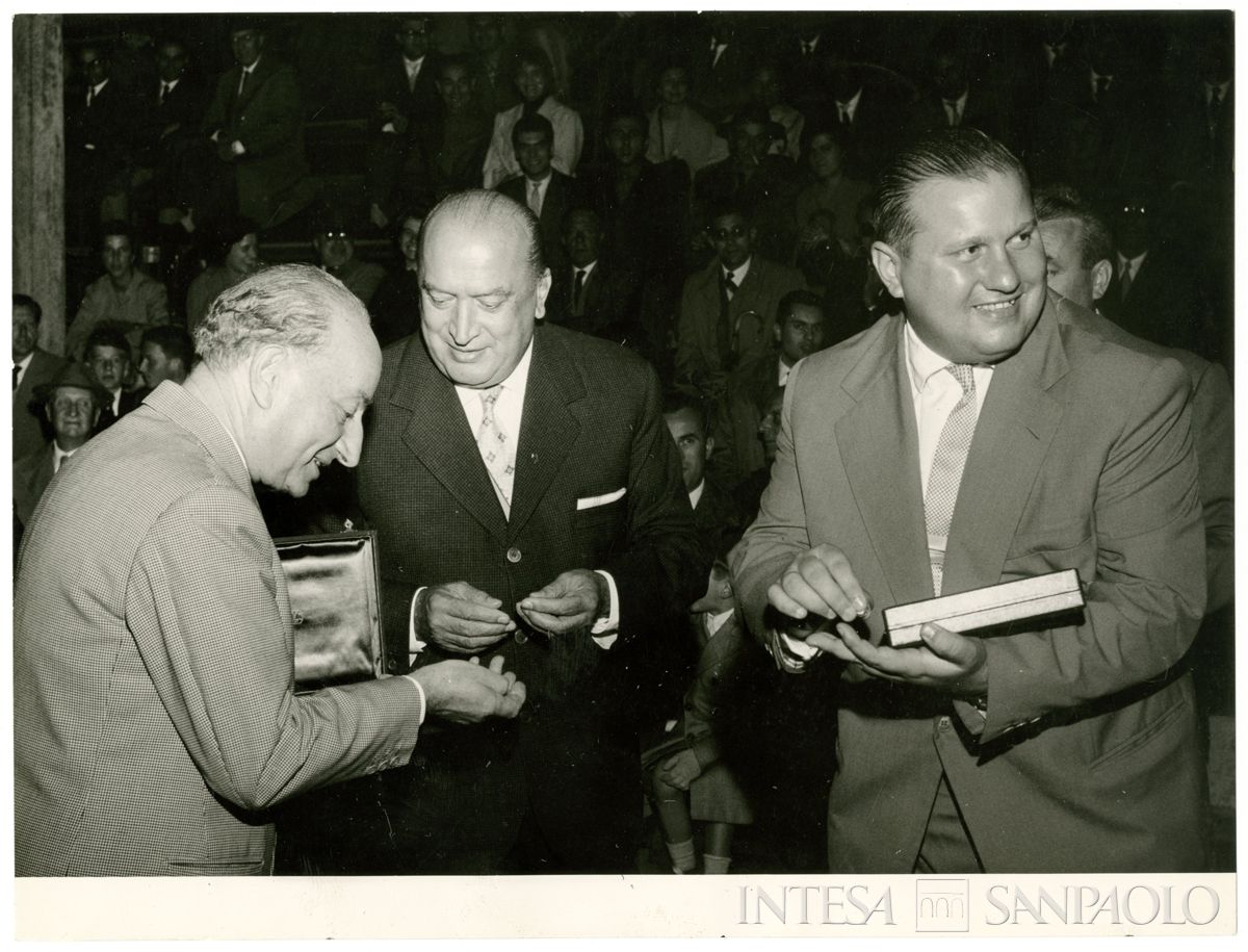 Carlo Alessandro Canesi, al centro, durante la consegna di spille e probabilmente medaglia/targa a due partecipanti alla manifestazione sportiva presso il campo sportivo del Banco Ambrosiano a Milano, 1 ottobre 1958 (Publifoto)