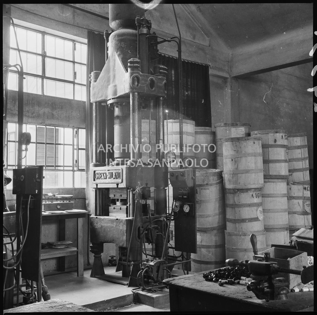 Primo piano di una pressa idraulica Chiesa presso lo stabilimento Aldo Leonetti. Sulla destra pile di barili di legno<br>24331