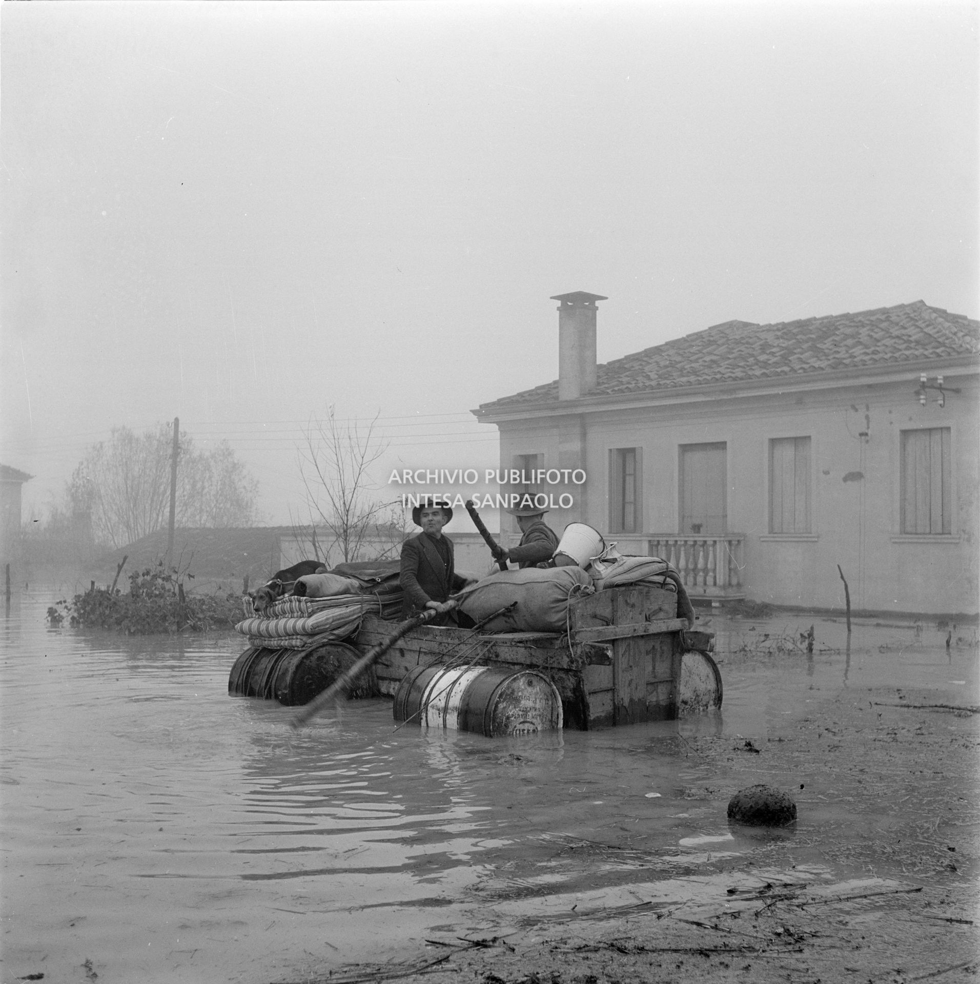 Due uomini a bordo di un mezzo di soccorso improvvisato durante l'alluvione nelle campagne del Polesine