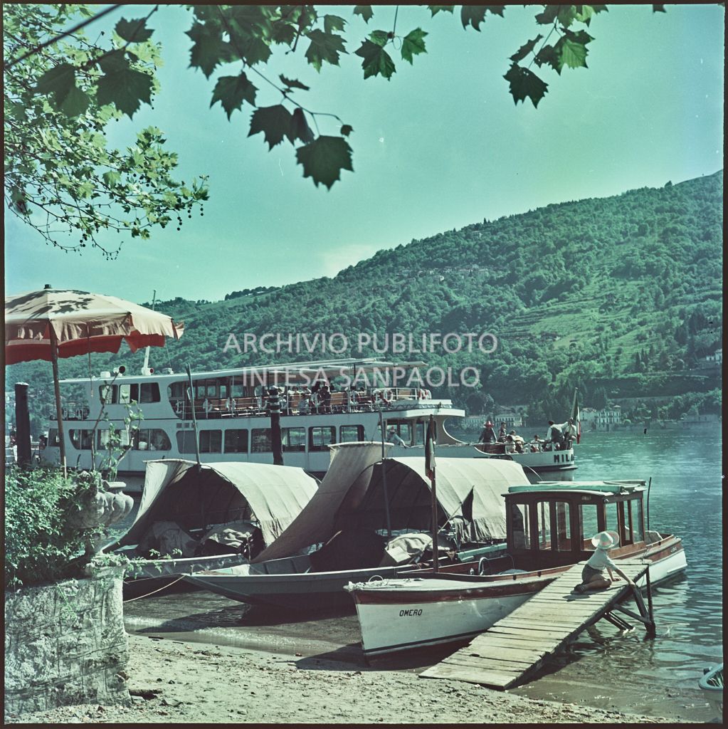 Vista dalla riva dell'Isola dei Pescatori sul lago Maggiore. In primo piano un molo, delle barche ed un traghetto<br>351