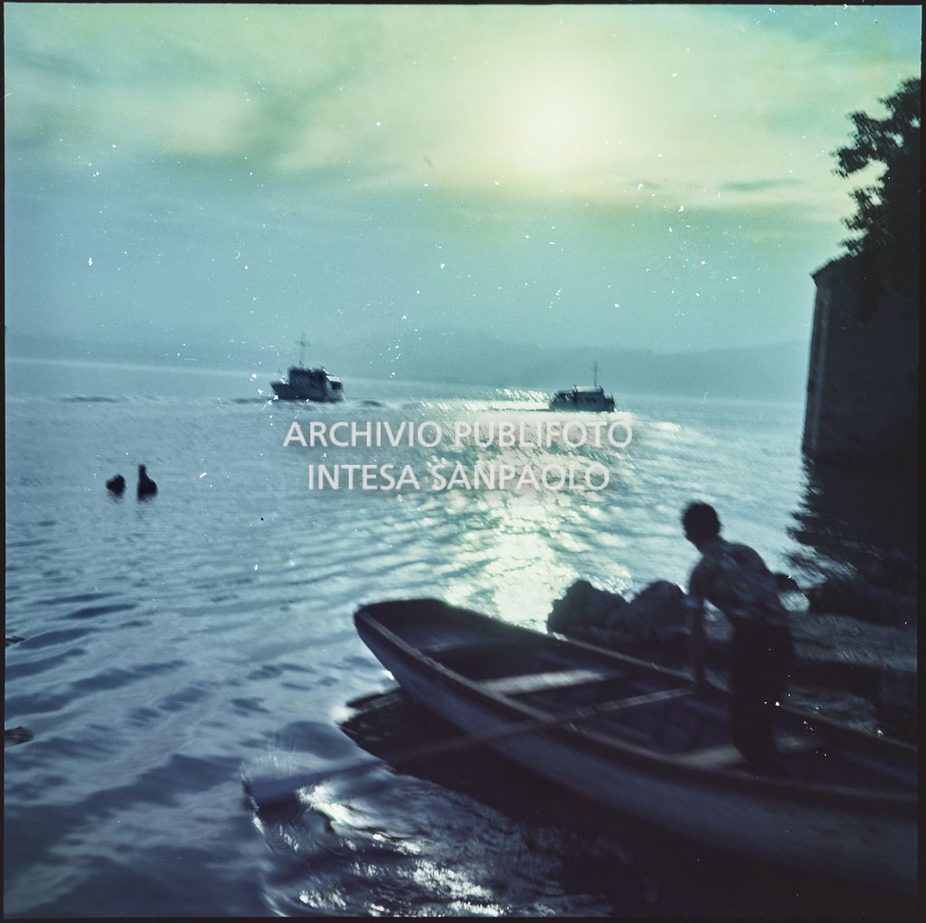 Uomo su una barca a remi al tramonto, in lontananza due imbarcazioni<br>368