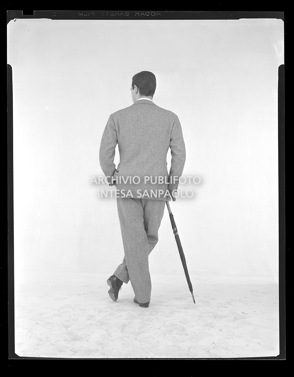 Uomo in abito elegante con pochette, cravatta e ombrello ripreso di spalle<br>14452