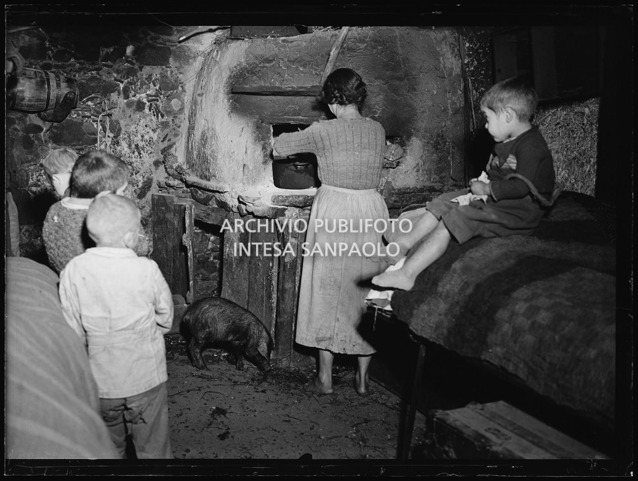 Africo, interno di una casa con bambini, una donna che cucina in un forno e un maiale