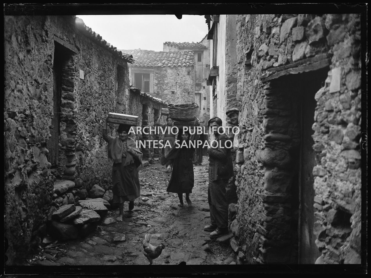 Africo, donne trasportano cesti sulla testa in una via del paese