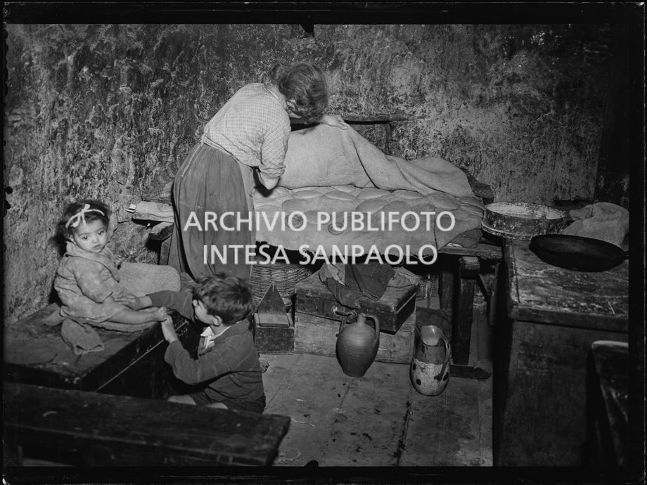 Africo, bambini e una donna davanti a delle forme di pane all'interno di una casa
