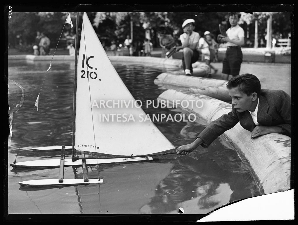 Un bambino gioca con il modellino di un catamarano nella fontana dei Giardini Pubblici di Milano