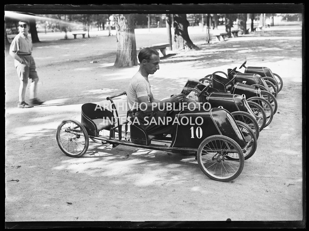 Un uomo legge una rivista seduto in un'automobilina a pedali ai Giardini Pubblici di Milano