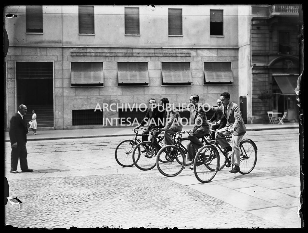Quattro uomini pedalano in gruppo in una via di Milano