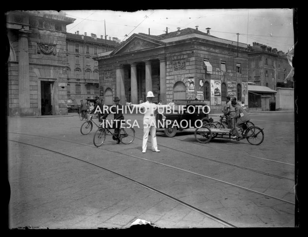 Un vigile regola la viabilità in piazzale Tommaso di Savoia (oggi piazza Venticinque Aprile) a Milano; alle sue spalle un casello di Porta Garibaldi