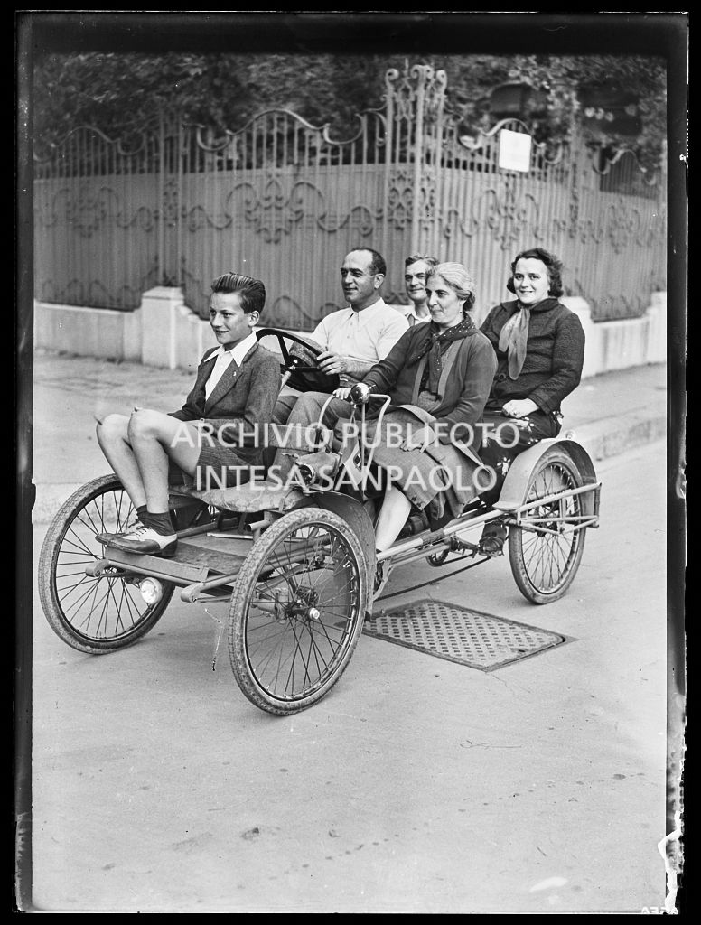 Quattro adulti e un ragazzo su un modello di automobile a pedali a Milano