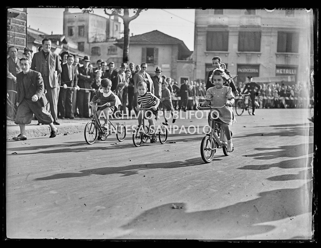 Corsa di bambini in bicicletta incitati dal pubblico assiepato lungo una strada a Milano