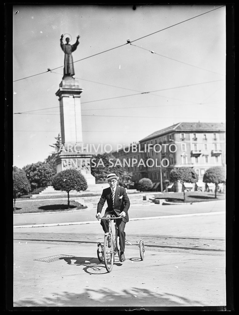 Un uomo, in abiti eleganti, in triciclo in piazza Risorgimento a Milano