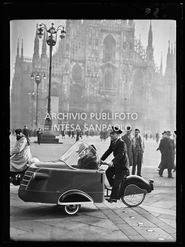 Due donne a bordo di un ciclo taxi in piazza del Duomo a Milano; sullo sfondo la cattedrale
