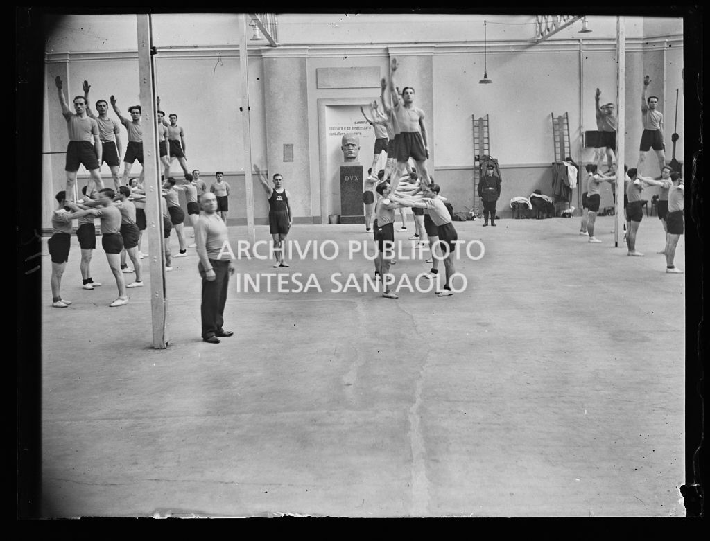 Un gruppo di ragazzi, alcuni dei quali eseguono il saluto romano, impegnato in un'esercitazione ginnica
