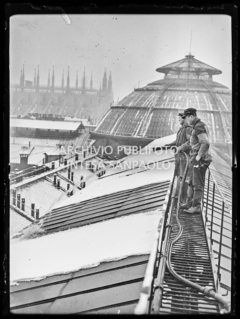 Due uomini spruzzano acqua con un idrante sulla copertura di vetro della Galleria Vittorio Emanuele II di Milano per liberarla dalla neve