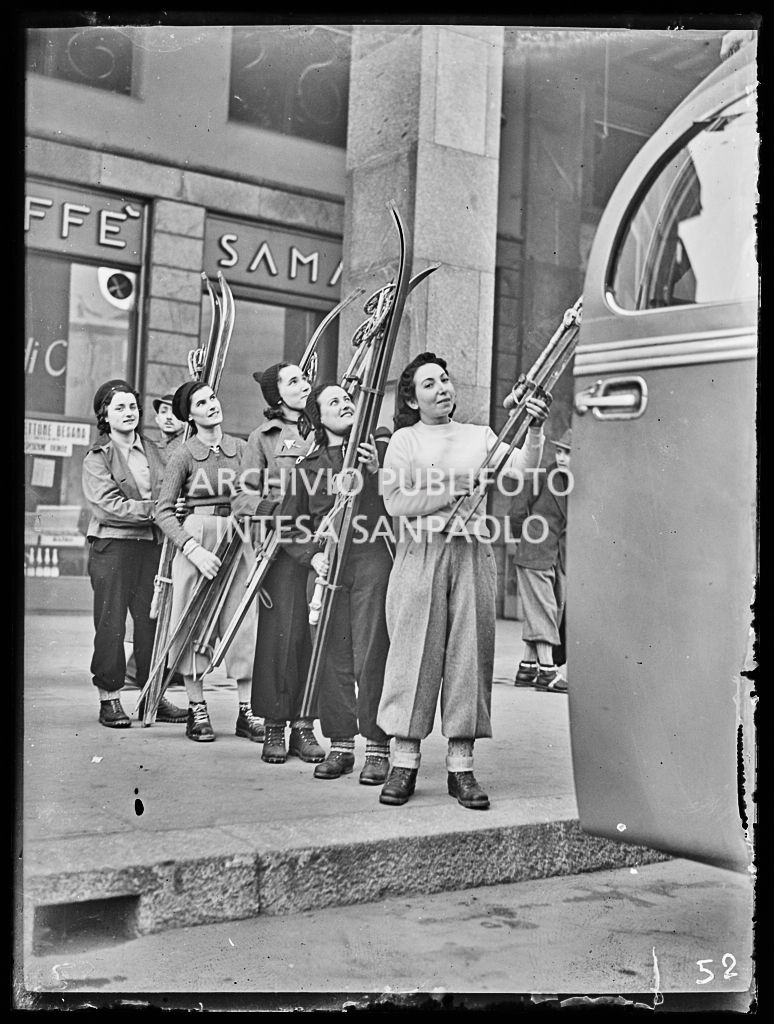 Ragazze in coda per salire su un pullmann imbracciano i loro sci