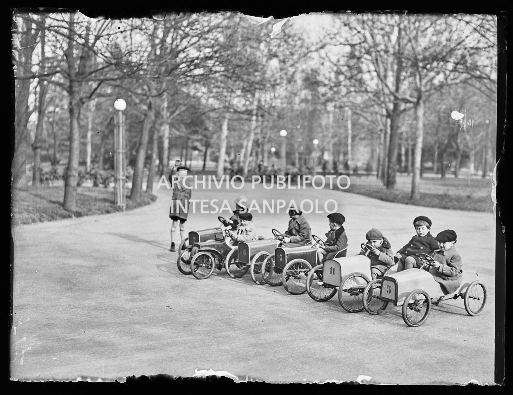 Un bambino dà il via ai suoi amici per una gara, a bordo di automobiline a pedali, in un parco