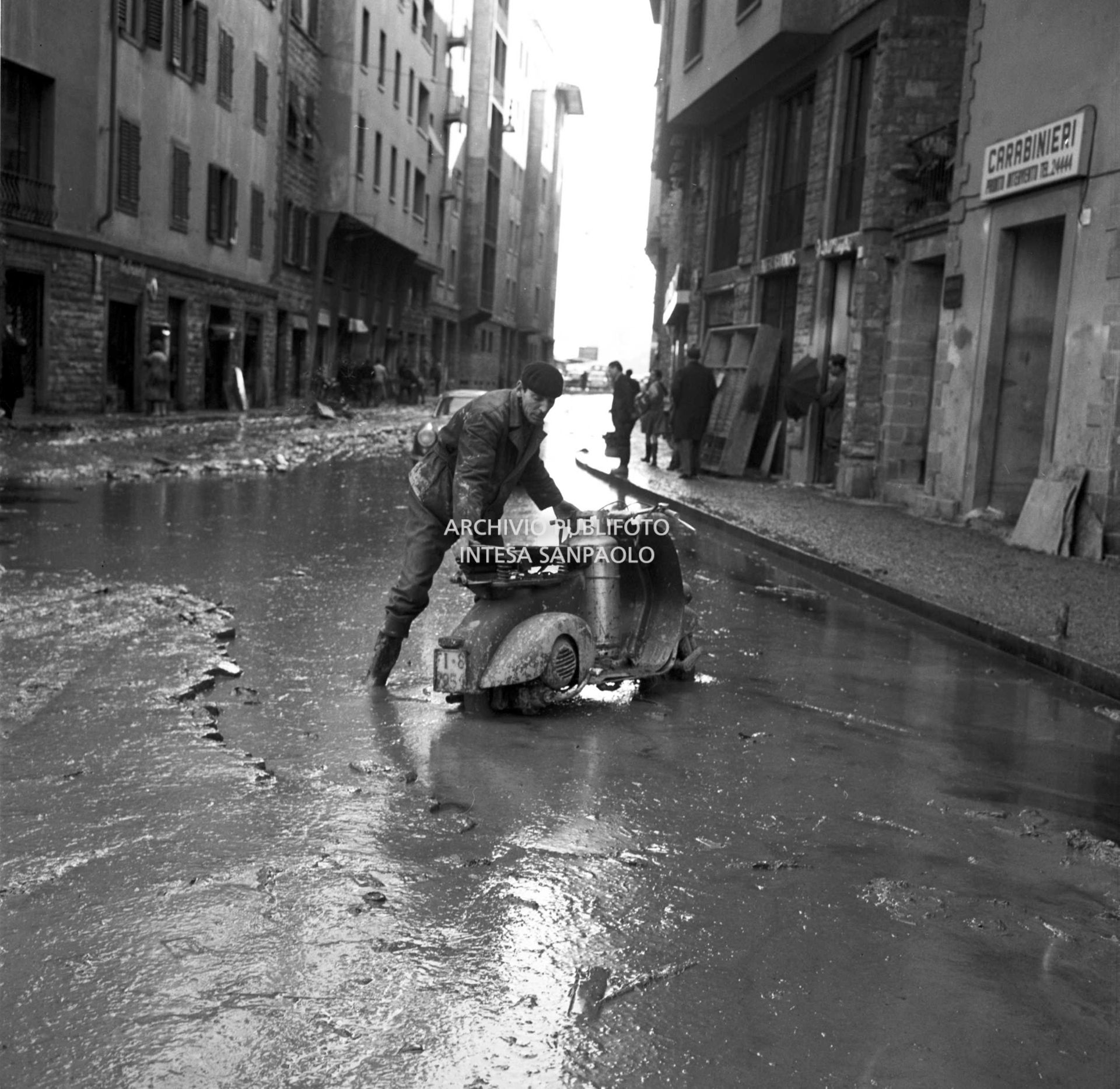 Alluvione di Firenze: un uomo spinge una Vespa, con a bordo una bombola di gas, nelle strade invase dal fango, dopo lo straripamento del fiume Arno