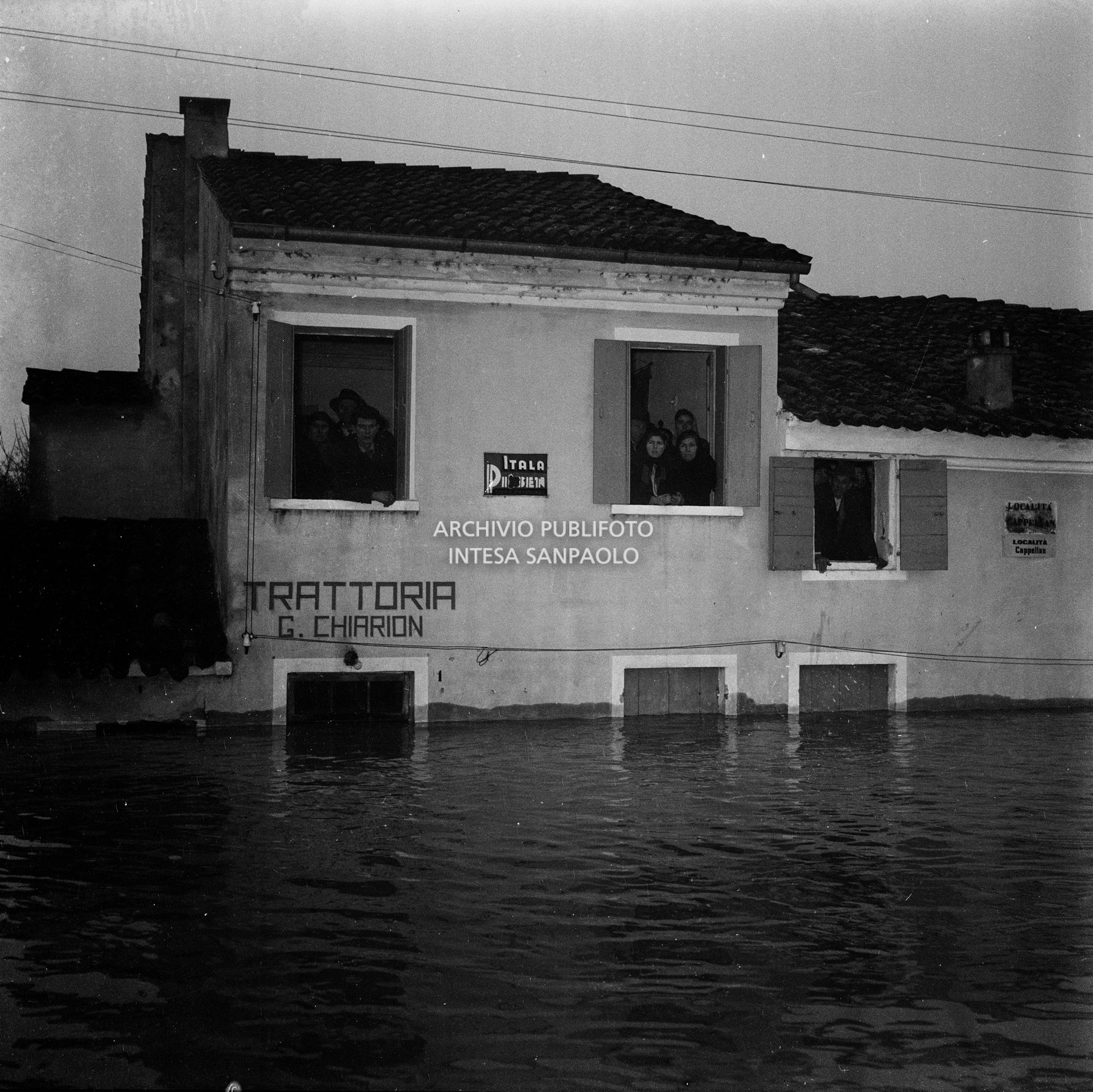 Persone affacciate alle finestre di un edificio parzialmente sommerso dall'acqua durante l'alluvione del Polesine