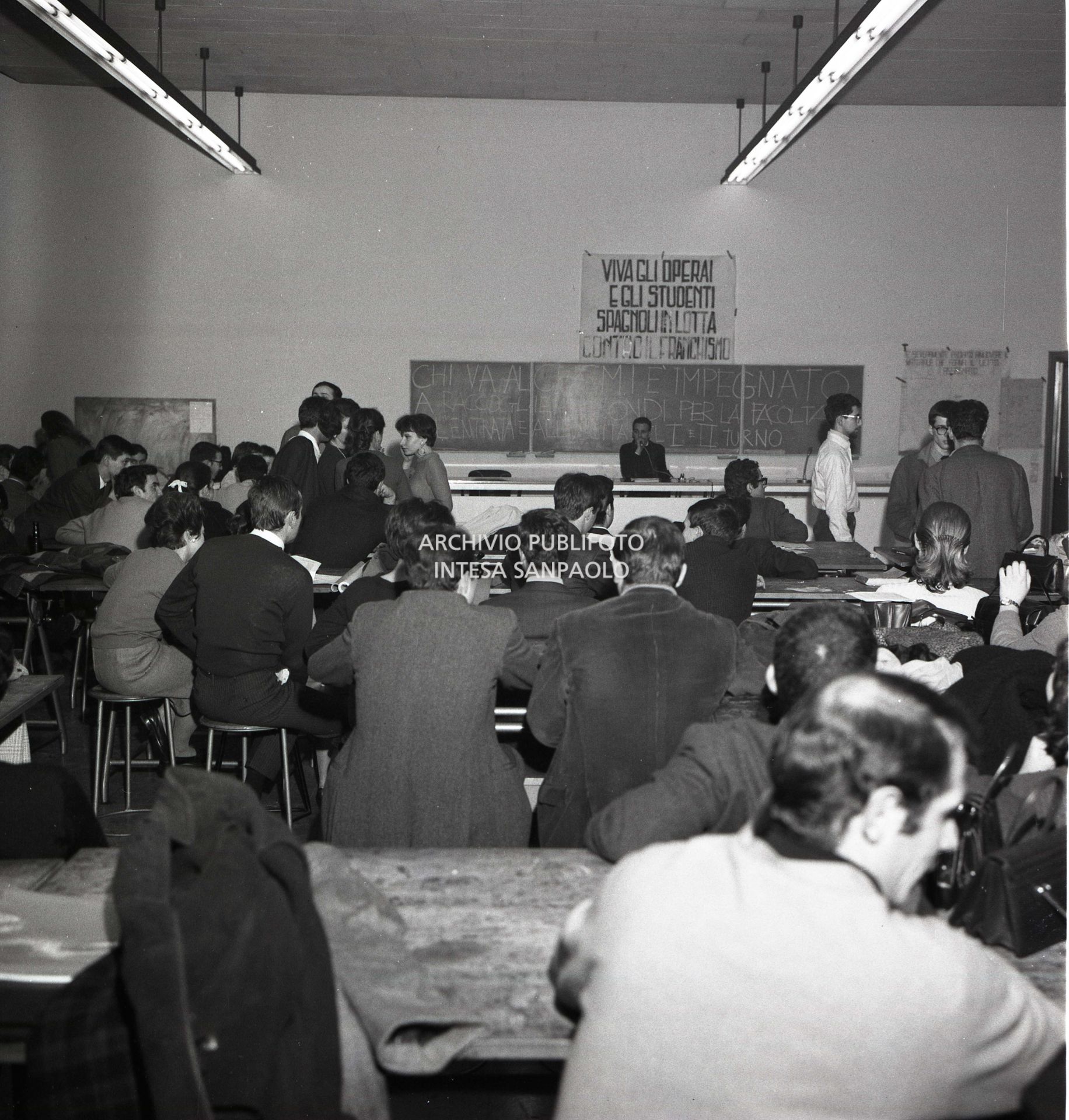 Studenti della Facoltà di architettura del Politecnico di Milano ripresi nel quarantunesimo giorno di occupazione dell'Ateneo. Sulla parete il cartellone con la scritta: "Viva gli operai e gli studenti spagnoli in lotta contro il franchismo".