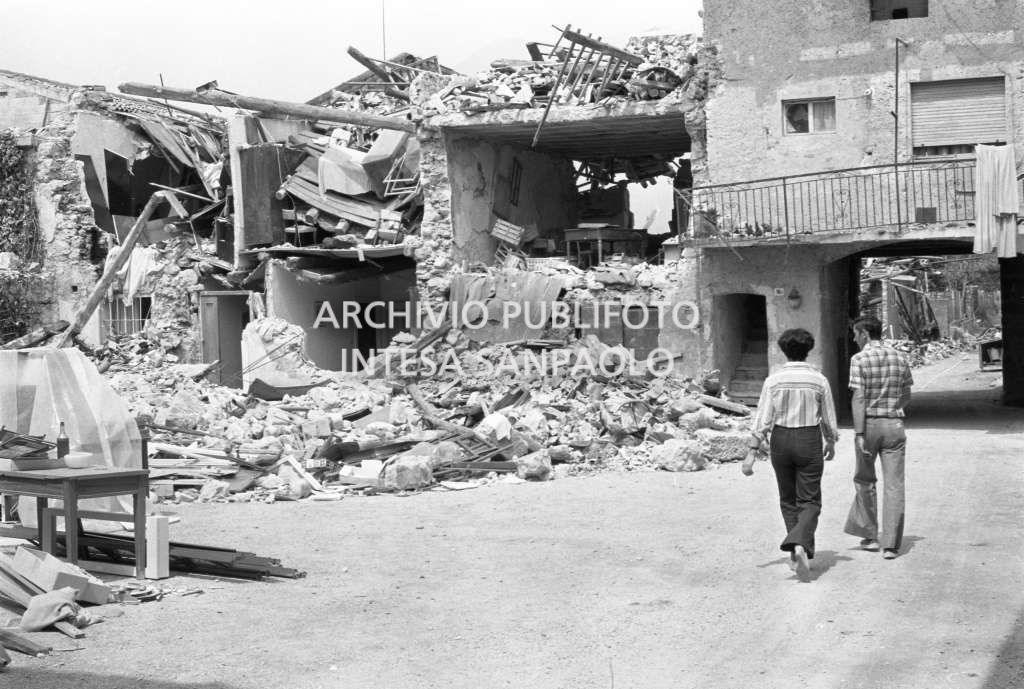 Due persone camminano in località colpita dal terremoto, visibili le macerie di alcune costruzioni