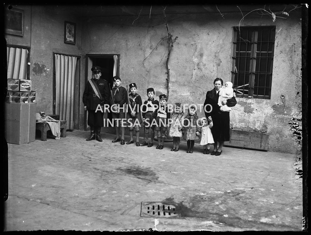 Una coppia, con i suoi otto figli, ritratta davanti all'entrata di casa; i figli maschi indossano divise da balilla e due di loro imbracciano il moschetto