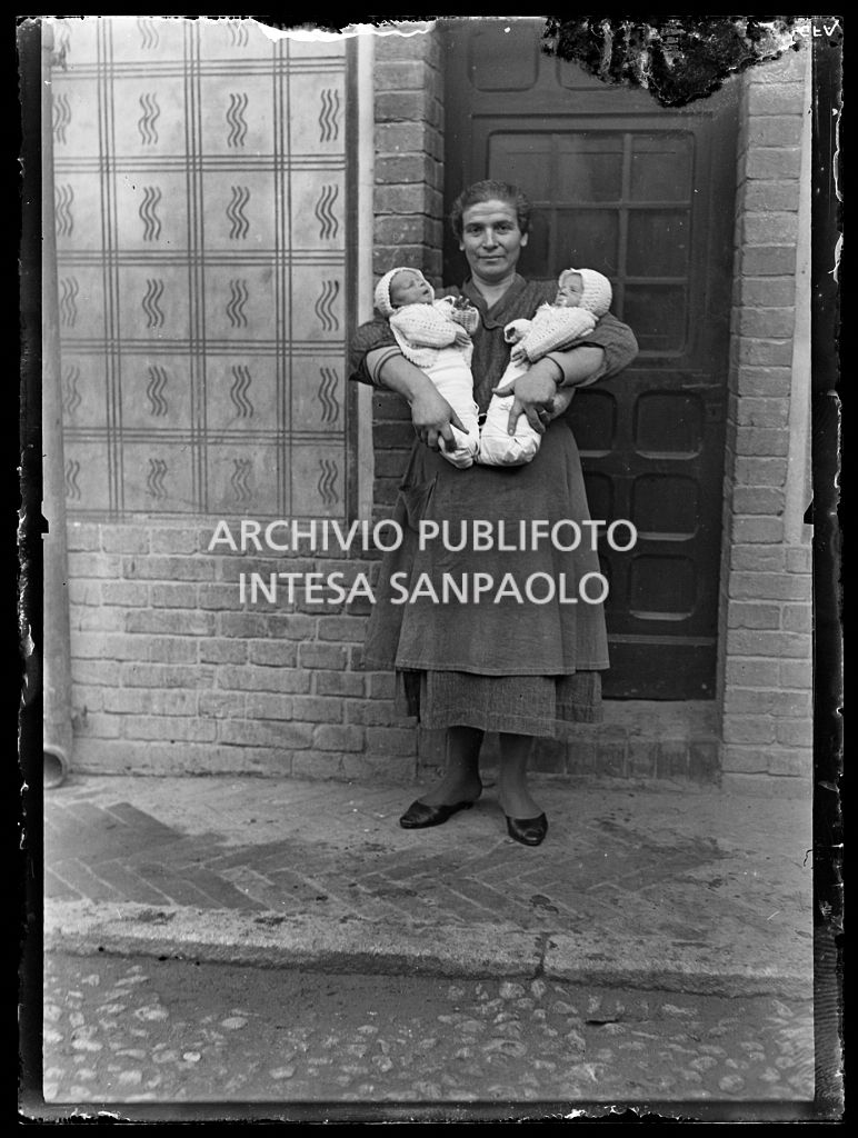 Una donna ritratta davanti a casa con due neonati in fasce