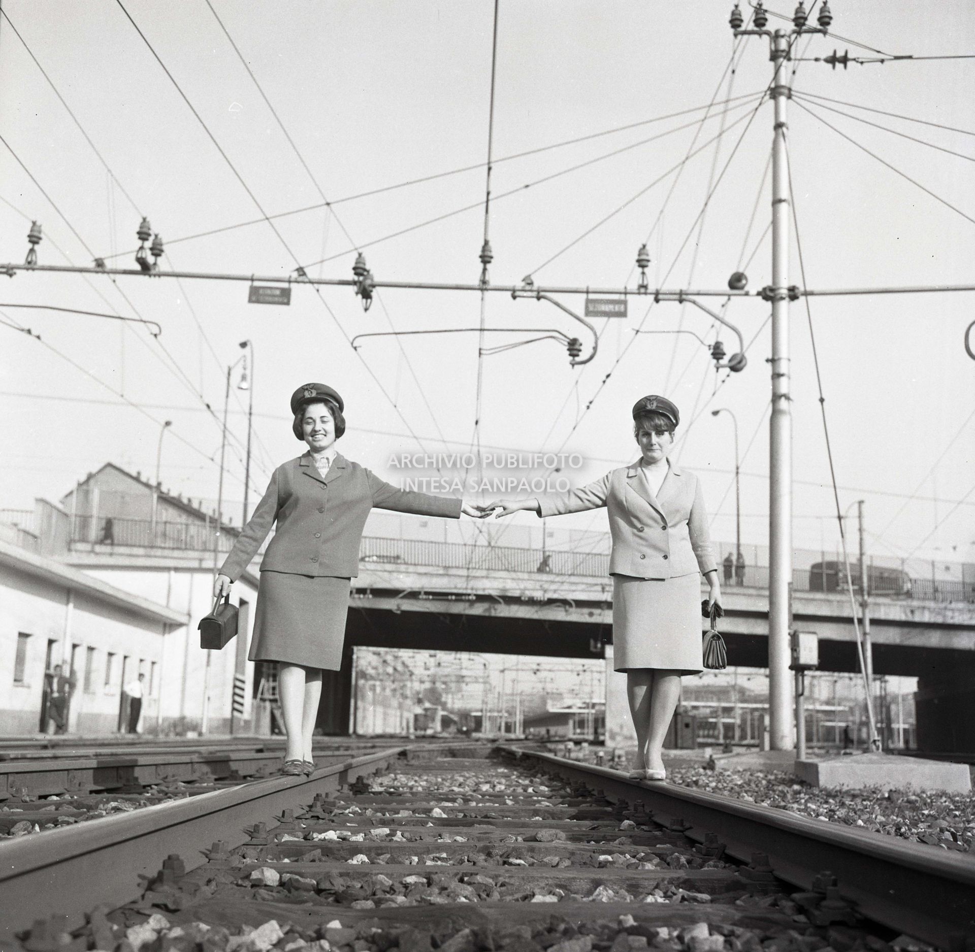 Simonetta Appolloni e Laura Lo Prieno, donne capostazione, si tengono per mano passeggiando sui binari ferroviari