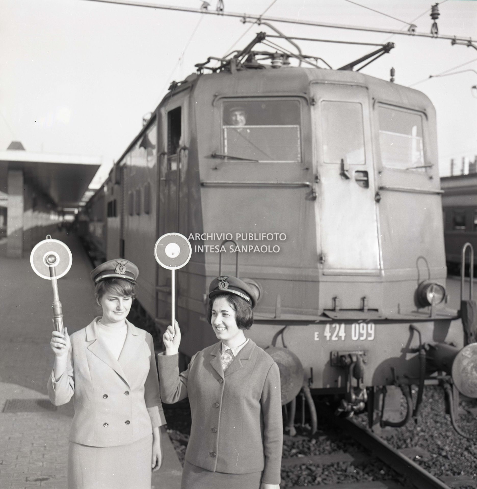 Simonetta Appolloni e Laura Lo Prieno, donne capostazione, in posa davanti a una locomotiva con la paletta d'ordinanza