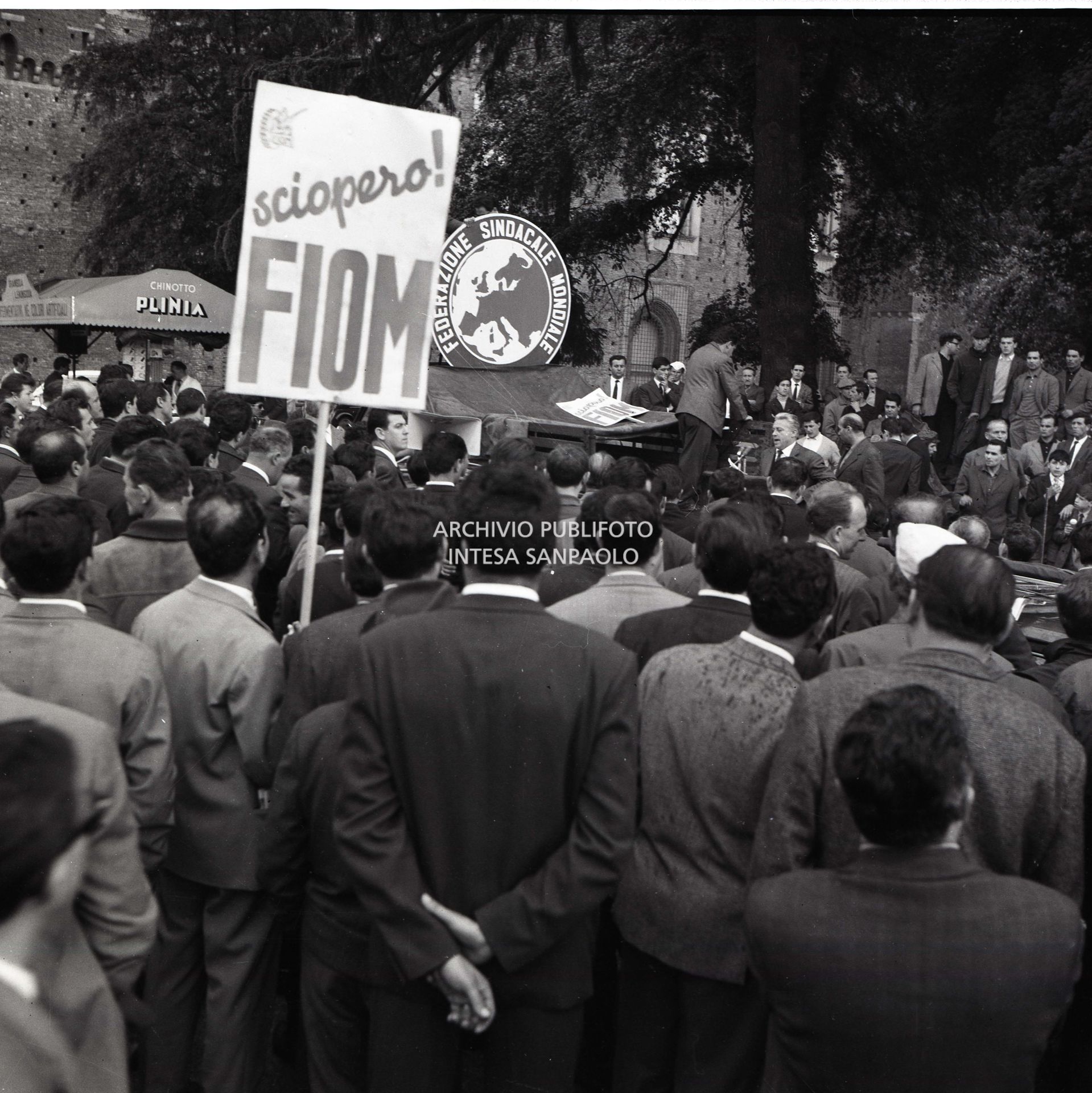 Sciopero CGIL: lavoratori in manifestazione con cartelli con la scritta "Sciopero FIOM". Sullo sfondo il simbolo della "Federazione sindacale mondiale".