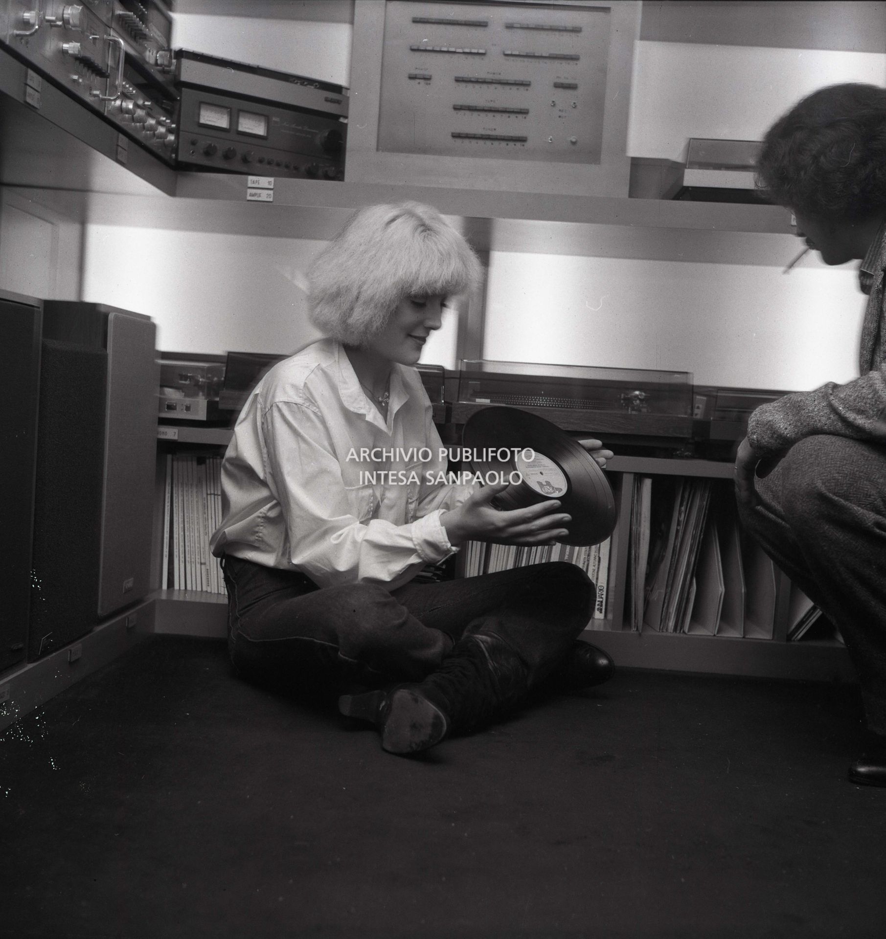 Donatella Rettore seduta per terra tiene in mano un LP in vinile; vicino a lei il fidanzato