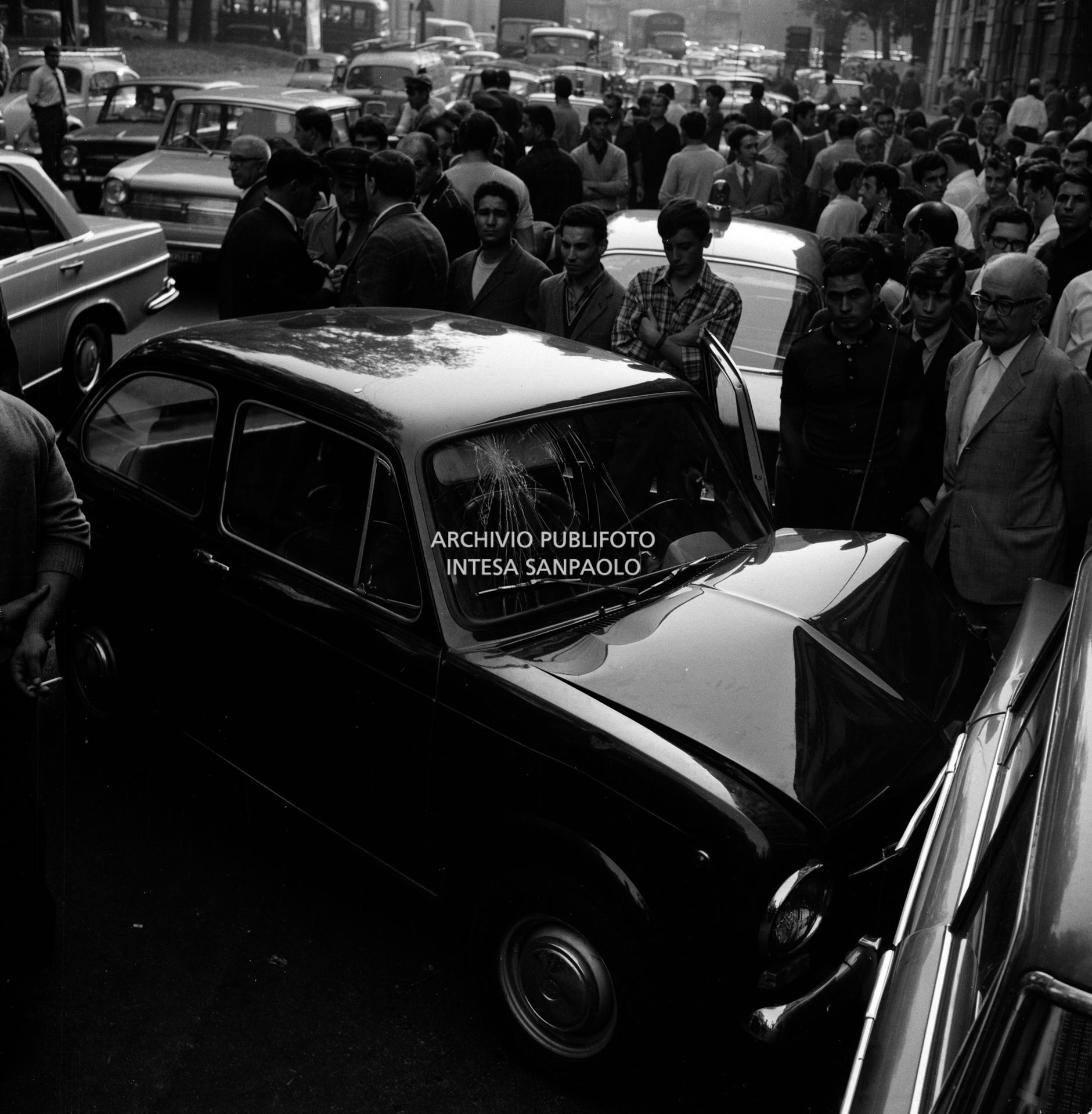 Folla di gente in via Bertani osserva la Fiat 850 che si è scontrata con una Fiat 1500 per evitare l'automobile dei banditi in fuga dopo la rapina all'agenzia del Banco di Napoli di largo Zandonai