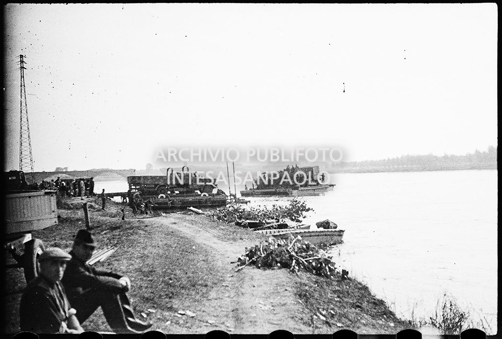 Due uomini seduti lungo l'argine del Po tra detriti e macerie dei bombardamenti; sullo sfondo il ponte sul fiume danneggiato<br>26657