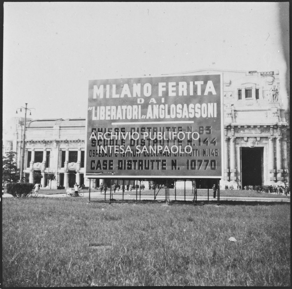 Grande cartello, posto davanti alla stazione Centrale di Milano, che elencava le distruzioni causate alla città dagli attacchi aerei dei "liberatori anglosassoni". Sullo sfondo la stazione.<br>26659 bis