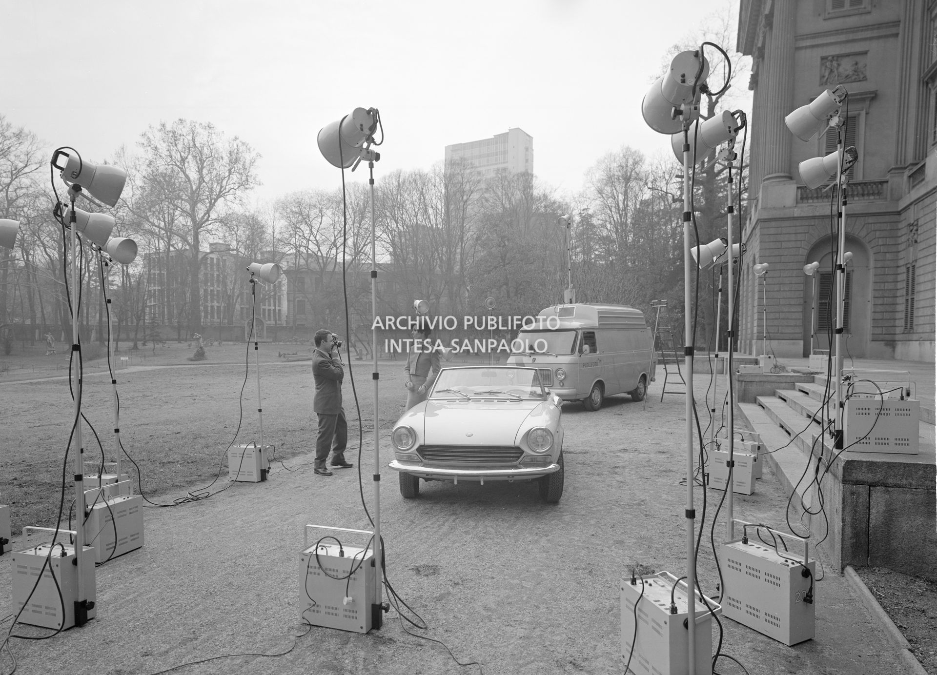 Set fotografico, dell'agenzia Publifoto, allestito nel giardino di Villa Reale a Milano: una modella ripresa accanto a una Fiat 124 Sport Spider