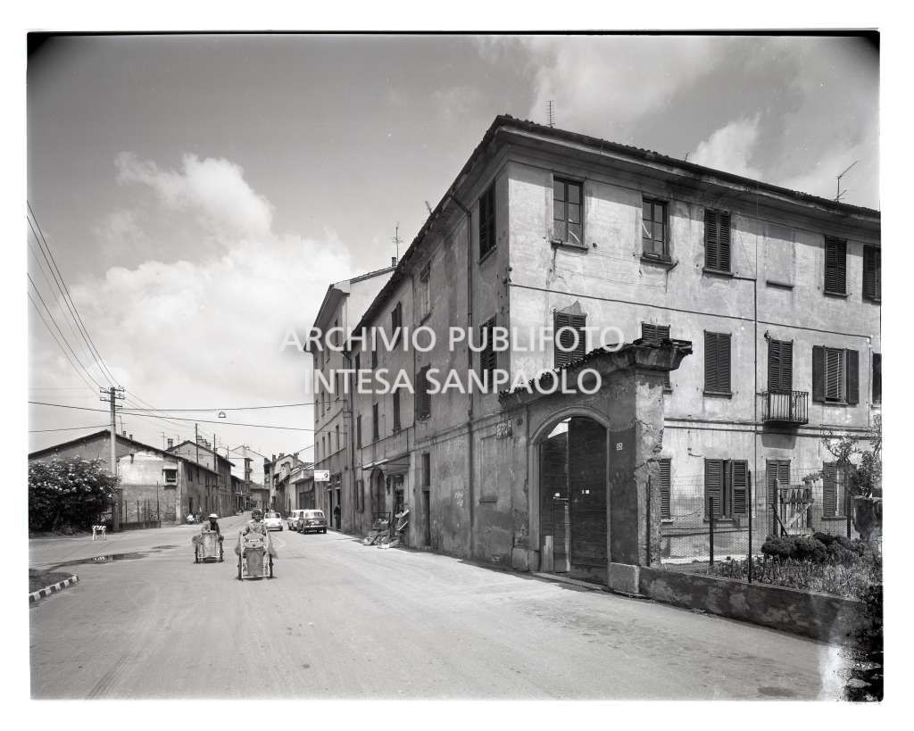 Bresso, due spazzini in una strada cittadina; sono visibili un fruttivendolo e un colorificio