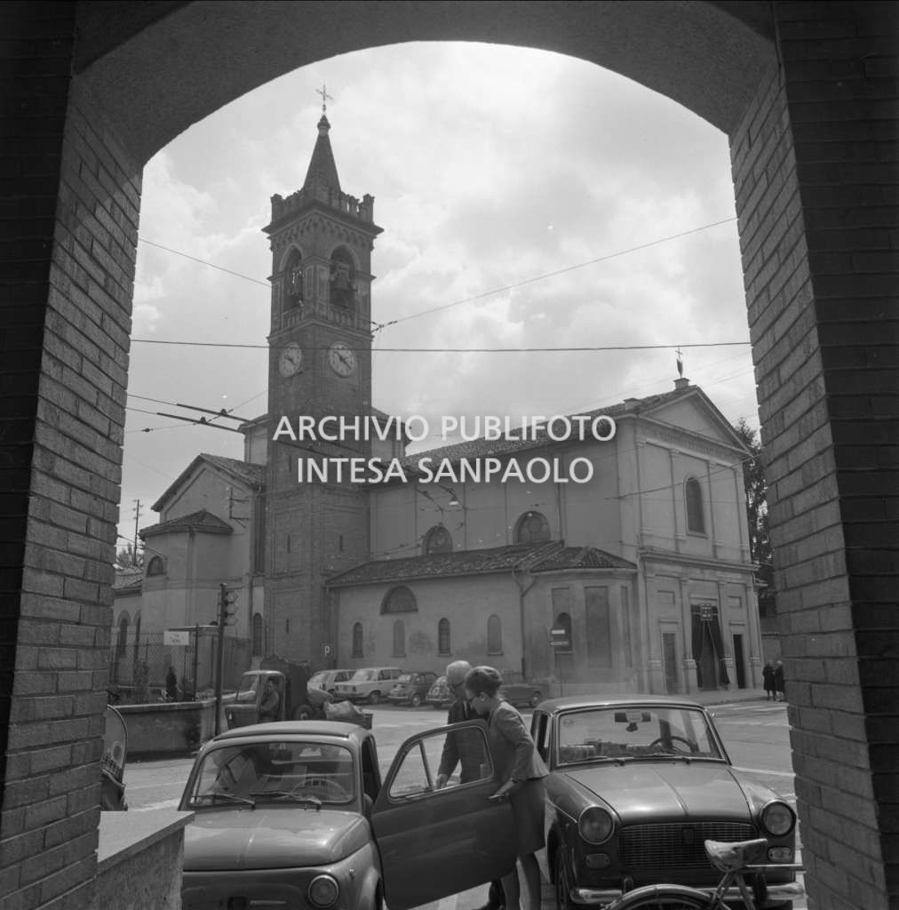 Bresso, la chiesa di San Nazaro e Celso, in via Roma, ripresa dall'entrata del Municipio; in primo piano un uomo e una donna accanto a un'automobile
